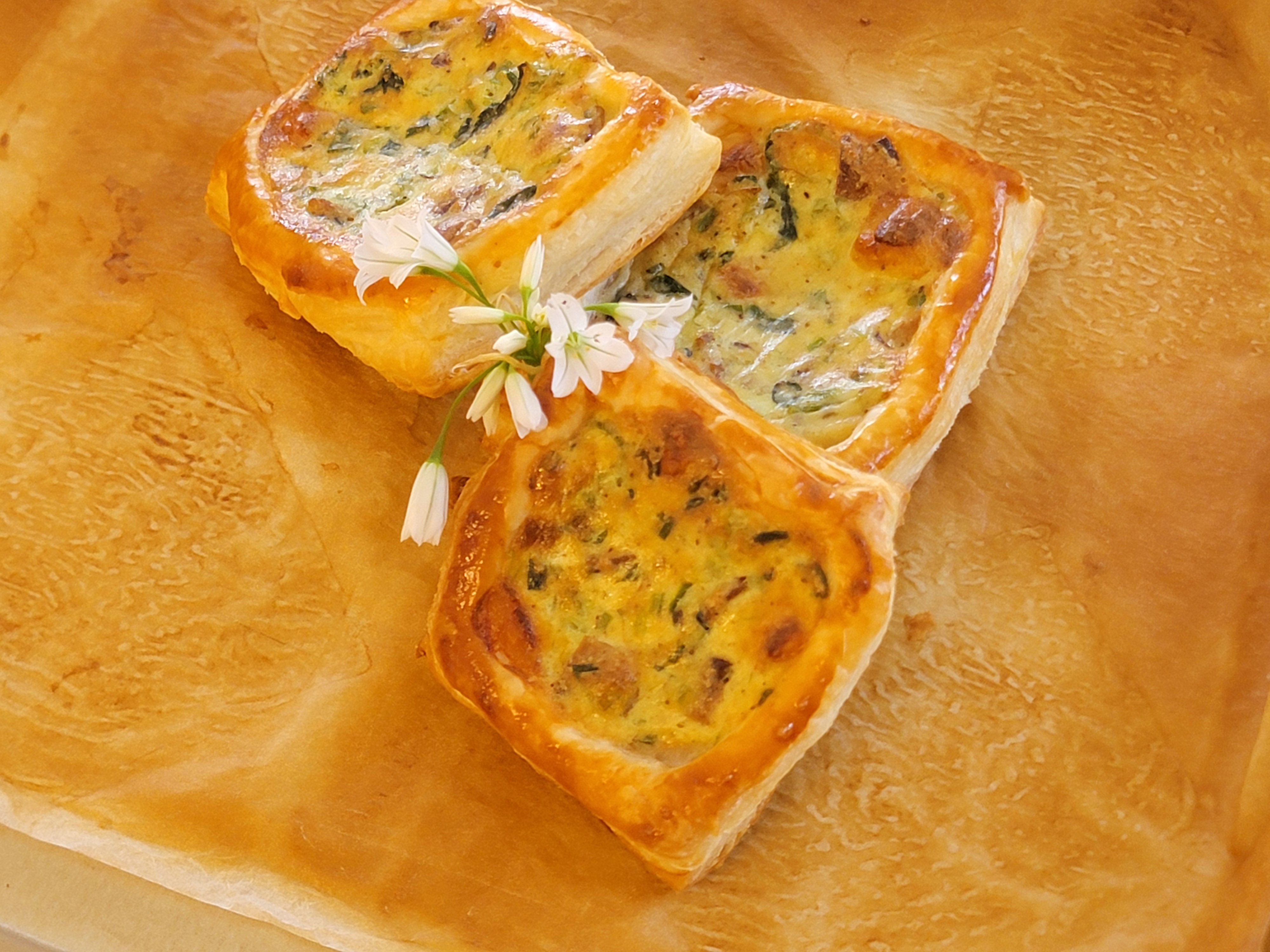 Three golden savory tarts filled with wild greens and garnished with three-cornered leek flowers